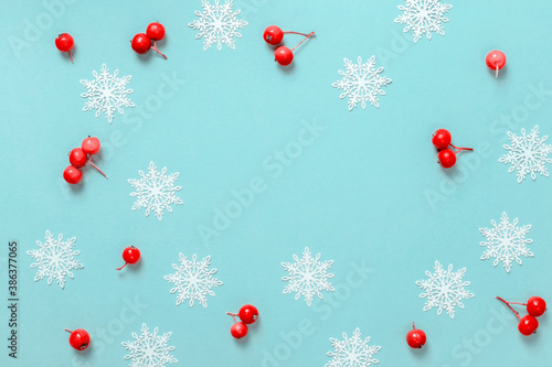 Xmas pattern. White snowflakes, red berry in Christmas composition on pastel blue background for greeting card. Flat lay, top view, copy space.