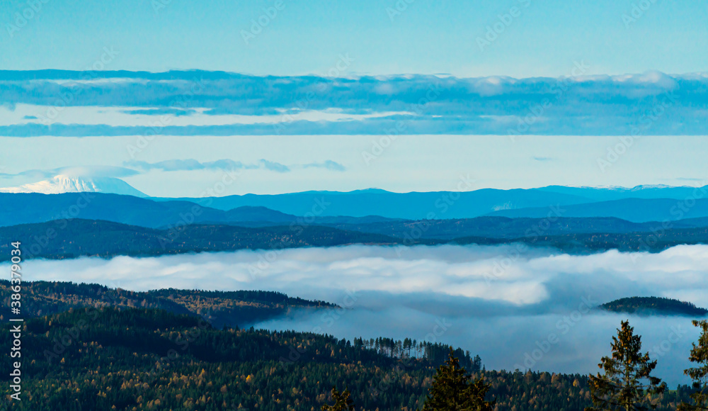 Fototapeta premium Morning fog in the valleys with a panoramic view over the boreal forest and snow covered mountains in the distance.