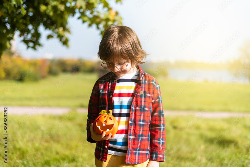 Cute boy in glasses play with pumpkin in autumn park on Halloween. Kids trick or treat. Fun in fall. Dressed up child Cute boy in glasses play with pumpkin in autumn park on Halloween. Kids trick or treat. Fun in fall. Dressed up child