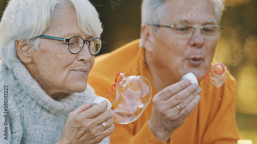 Romance at old age. Elderly couple blowing soap bubbles in the park in autumn. High quality photo