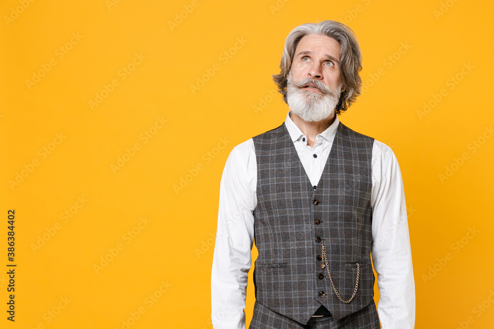 Pensive elderly gray-haired mustache bearded business man in checkered suit waistcoat white shirt standing looking up isolated on yellow background studio portrait. Achievement career wealth concept.