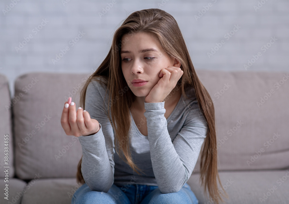 Young woman feeling depressed, looking at pill, thinking of committing suicide, indoors - obrazy, fototapety, plakaty 