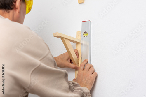 Canvastavla A man hangs a shelf in an apartment on a white wall, a worker checks the evennes