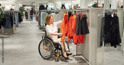 Woman shopper in a wheelchair chooses clothes in the mall. Christmas gifts, new year sale