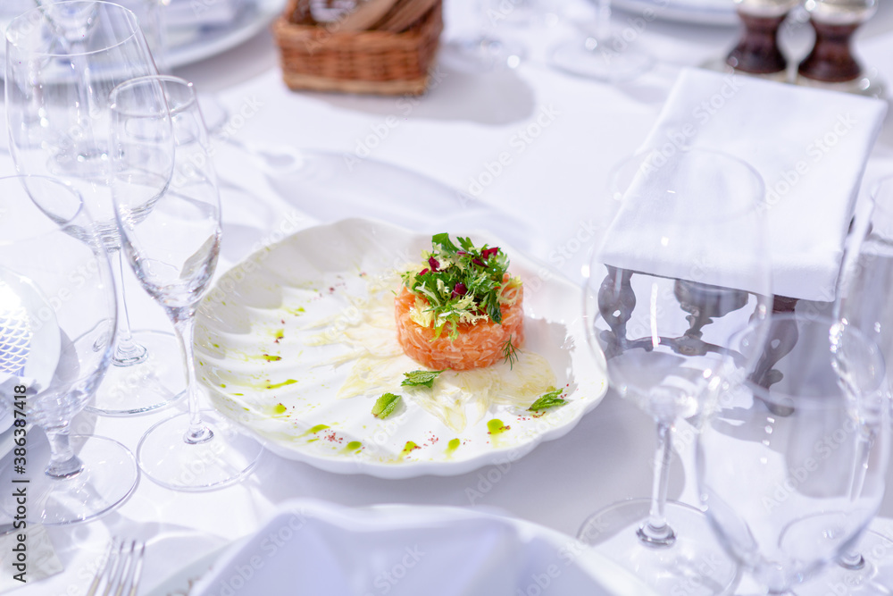 salmon dish on a white plate with glasses on a white tablecloth