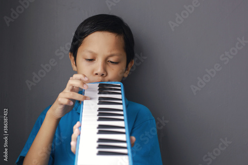 Boy playing blue melodeon musical instrument, melodica blow organ, pianica or melodion on dark gray background photo