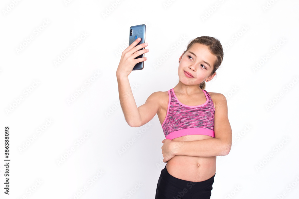 Pretty young sport and healthy girl in fitness dress makes selfie with mobile phone. Isolated photo on white background with copy space. Pretty young sport and healthy girl in fitness dress makes selfie with mobile phone. Isolated photo on white background with copy space.