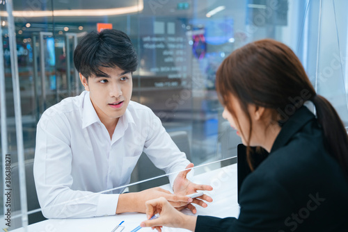 Asian man talking with receptionist for advice.