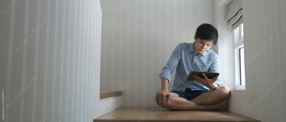 A young man using tablet while sitting on a staircase at home.