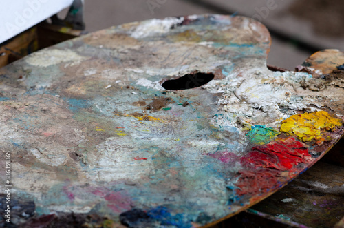 wooden palette for mixing paints on an easel smeared with multi-colored oil paints