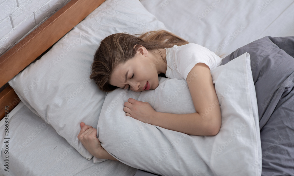 Top view of depressed young woman lying in bed and hugging her pillow Top view of depressed young woman lying in bed and hugging her pillow