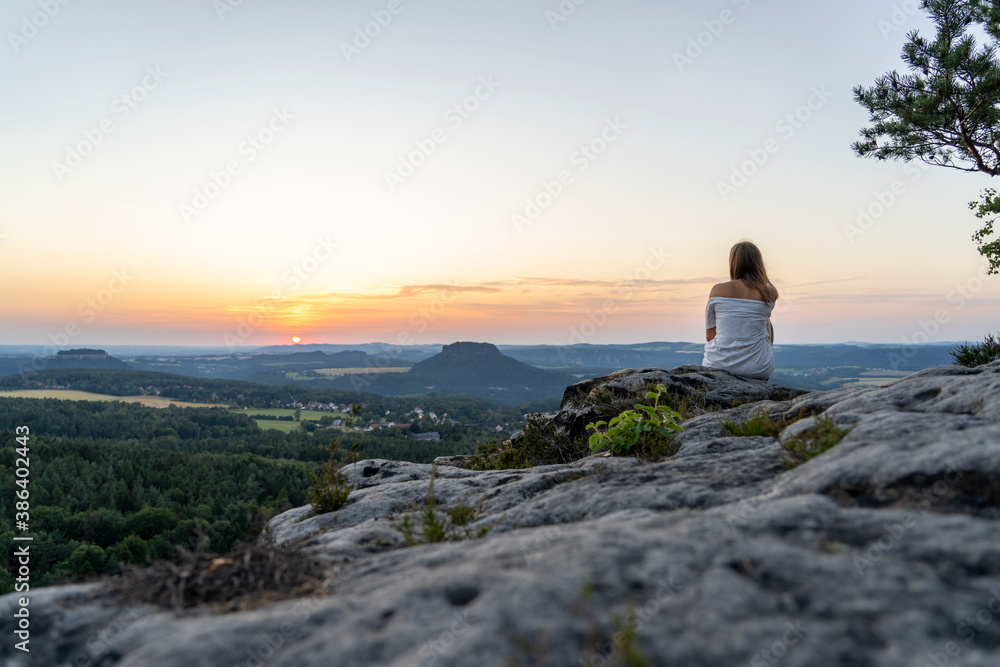Junge Frau sitzt auf Steinen mit Blick zum Sonnenuntergang