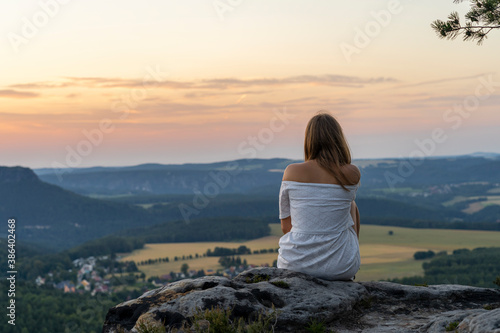 Junge Frau sitzt auf Steinen mit Blick zum Sonnenuntergang © Denis