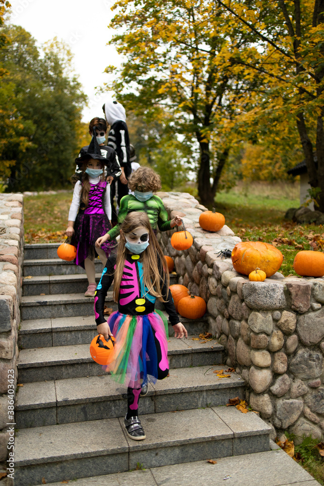 Group of trick-or-treating kids wearing face masks walking down the stairs. Halloween celebration during COVID-19 coronavirus pandemic Group of trick-or-treating kids wearing face masks walking down the stairs. Halloween celebration during COVID-19 coronavirus pandemic