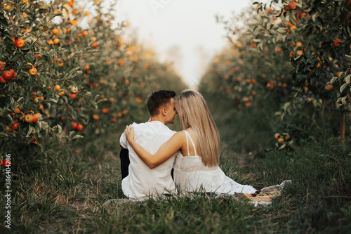 Obraz na płótnie Happy couple together are relaxing and drinking wine at summer picnic in the apples orchard. Back view. w salonie