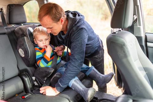 Father fastening safety belt for his baby boy in his car seat. © len44ik