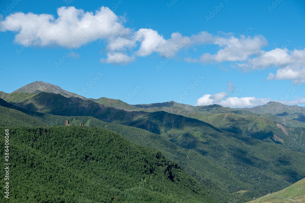 Fototapeta premium Panoramic view on a mountain range covered by green forest and view on ruins of upper Chazhash Castle, Upper Svaneti, Georgia