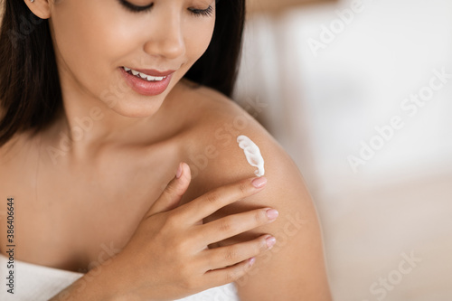 Closeup of asian lady wrapped in towel moisturizing her skin