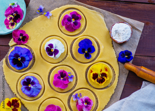 Shortcrust pastry dough decorated with natural edible flowers on dark wooden background