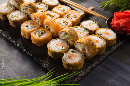 Set of baked sushi rolls with wasabi and ginger on black