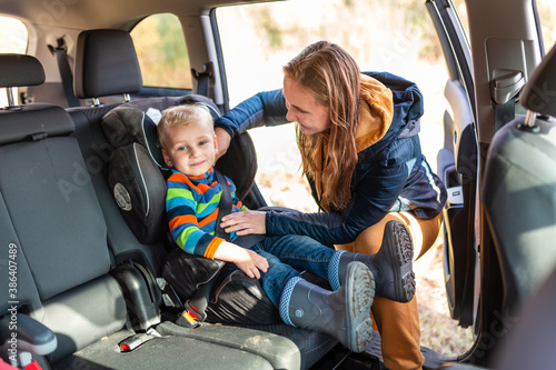 Fotografie Mother fastening safety belt for her baby boy in his car seat.