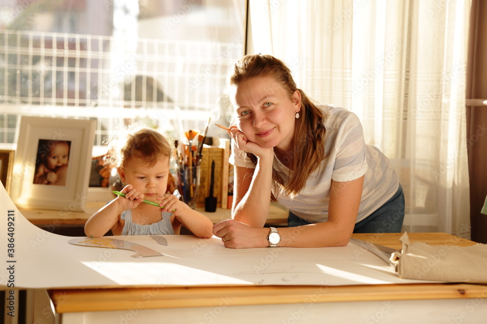 Beautiful woman cutting dress patterns in home with her little cute girl Beautiful woman cutting dress patterns in home with her little cute girl