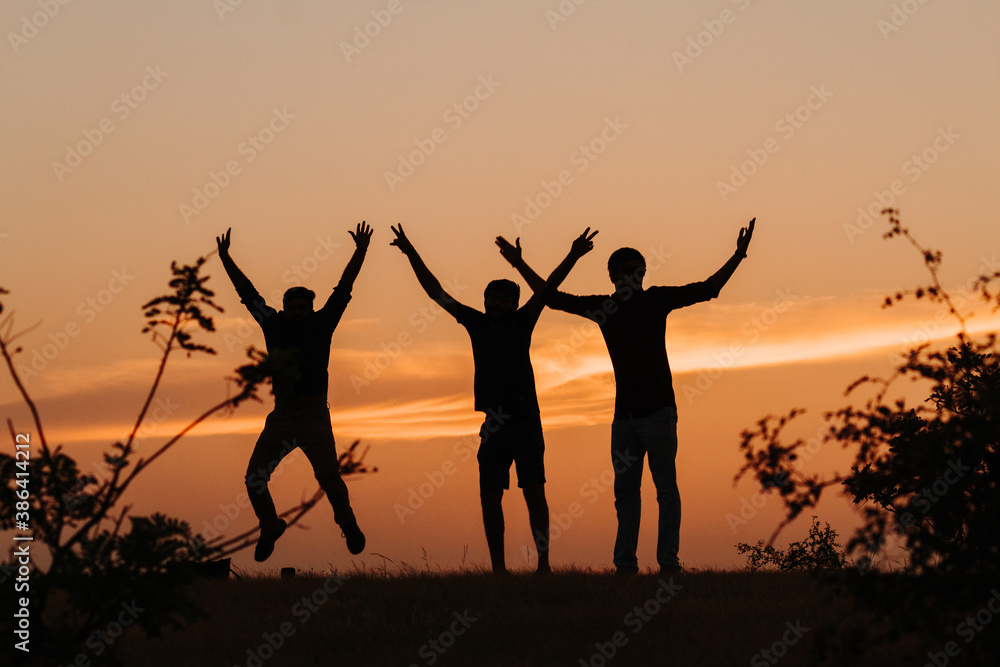 Silhouette of three Indian friends jumping with arms raised against the sky during the sunset