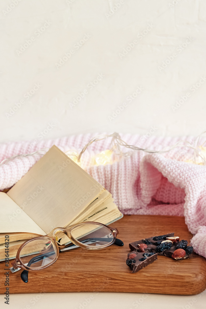 Flat lay composition with open blank paper notebook glasses and natural black chocolate bar with nuts and dried fruits near white knitted blanket and fairy lights. Flat lay composition with open blank paper notebook glasses and natural black chocolate bar with nuts and dried fruits near white knitted blanket and fairy lights.