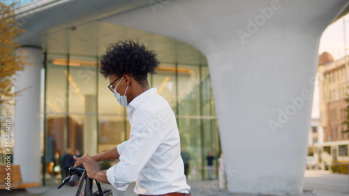 Portrait of afro american businessman in mask leaving business center and riding away on scooter