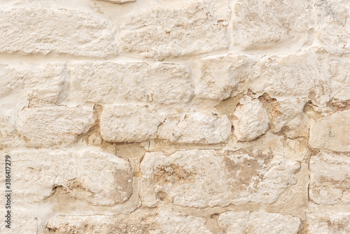 Old fashioned surface of historical building wall made of weathered brown bricks covered with white flaked stucco at bright sunlight extreme close view