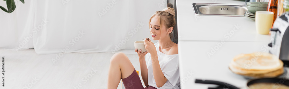 website header of young blonde woman eating cornflakes while sitting on floor in kitchen website header of young blonde woman eating cornflakes while sitting on floor in kitchen