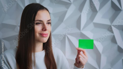 Beautiful brunette girl smiles and shows an element for advertising, with a green screen, on a white volumetric background