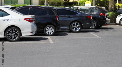 Closeup of rear side of white car with other cars parking in outdoor parking area in bright sunny day. 