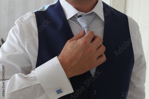 groom setteling his gray coloured tie while wearing a dark blue vest