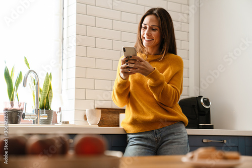 Beautiful caucasian woman smiling and using cellphone in apartment photo