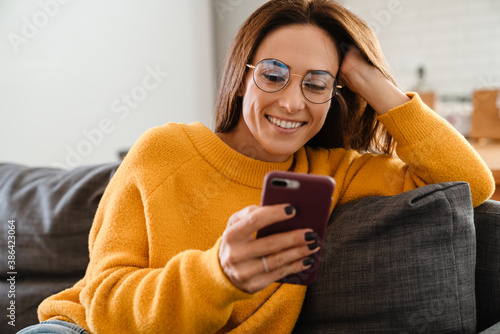 Beautiful woman smiling and using cellphone on sofa in apartment photo