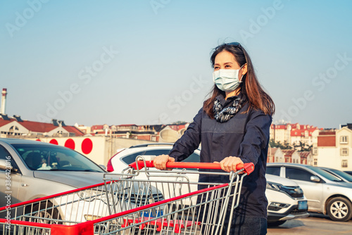 Woman shopping with hand pushing cart in supermarket parking lot