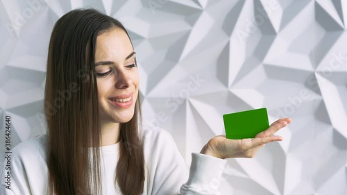 Beautiful brunette girl smiles and shows an element for advertising, with a green screen, on a white volumetric background