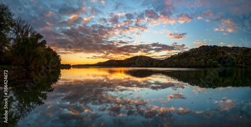 Dramatic clouds in a colorful sunset sky are reflected on the beautiful Ohio River, as photographed from Paden City, West Virginia, with the hills along the valley displaying beautiful autumn leaves. photo