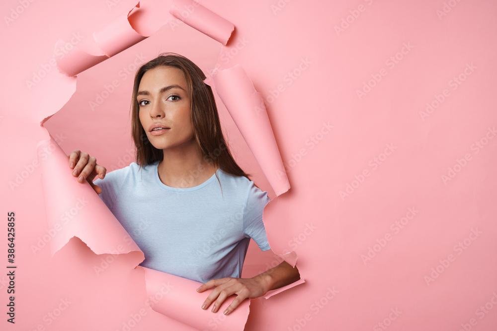 Fototapeta premium Young brunette woman in t-shirt posing isolated over pink background