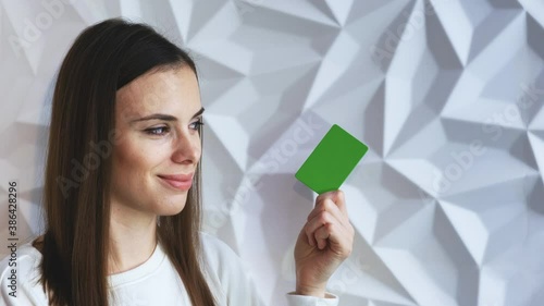 Beautiful brunette girl smiles and shows an element for advertising, with a green screen, on a white volumetric background