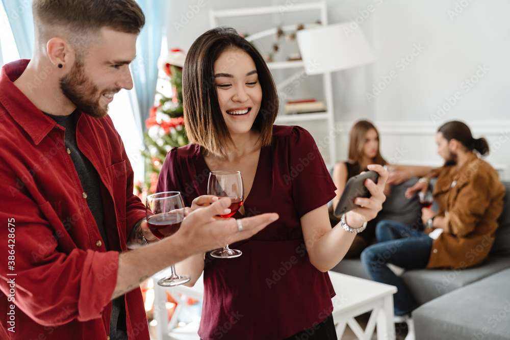 Image of joyful multinational friends using cellphone while drinking wine