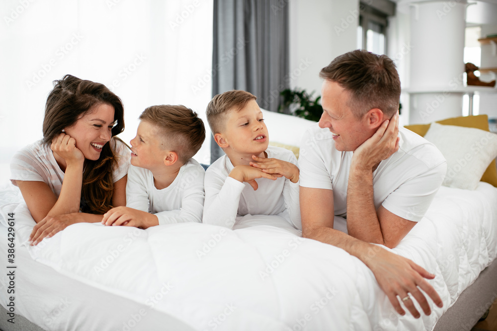 Fototapeta premium Young family enjoying in bed. Happy parents with sons relaxing in bed.