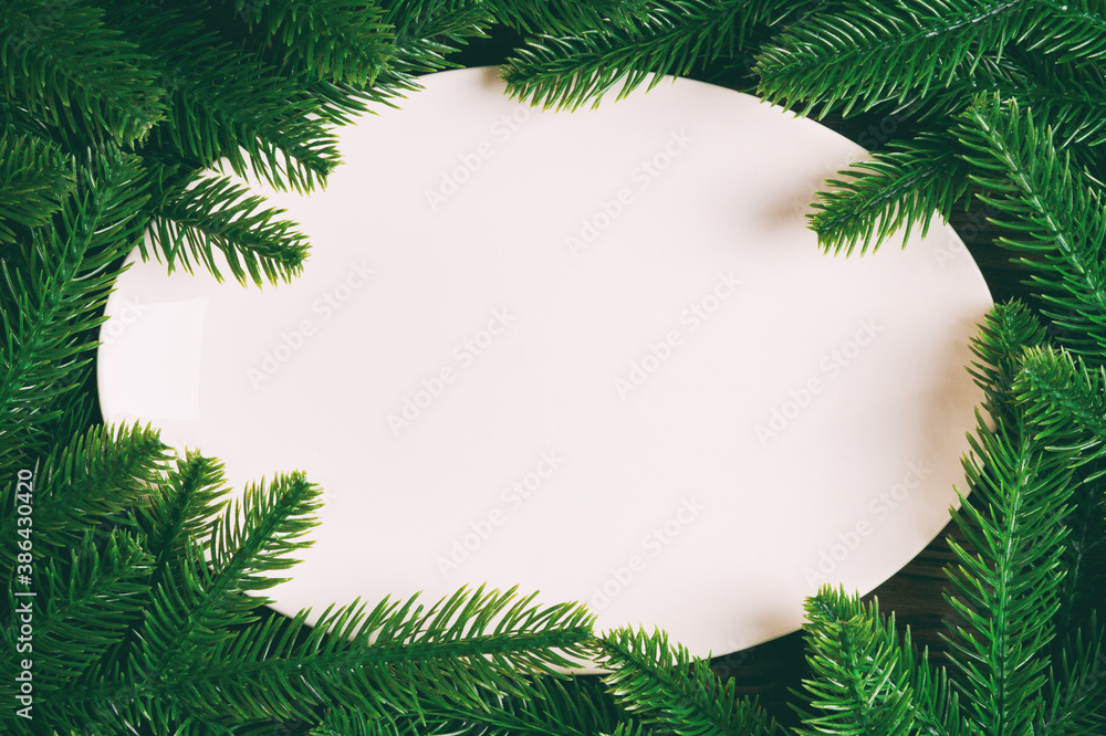 Top view of white plate surrounded with fir tree branches. Christmas dinner concept with copy space