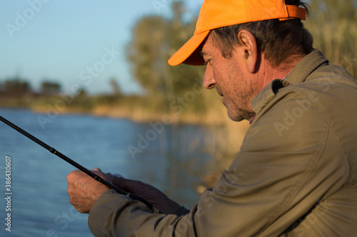 Fishing rod wheel closeup, man fishing with a beautiful sunset.