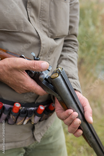 Close up of hunter loading shotgun, holds a gun and ammunition in his hand.