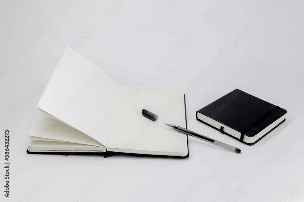 Black small closed square notepad and large open notebook with blank white pages and gel pen with cap. Empty paper. Office book Black small closed square notepad and large open notebook with blank white pages and gel pen with cap. Empty paper. Office book