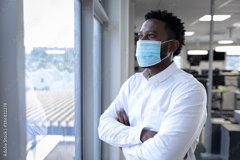 Businessman wearing face mask looking through window at modern office Businessman wearing face mask looking through window at modern office