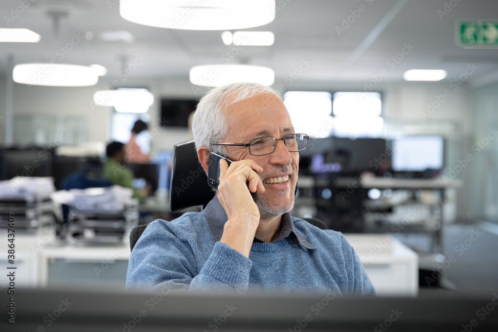 Senior businessman talking on smartphone while sitting on his desk at modern office Senior businessman talking on smartphone while sitting on his desk at modern office