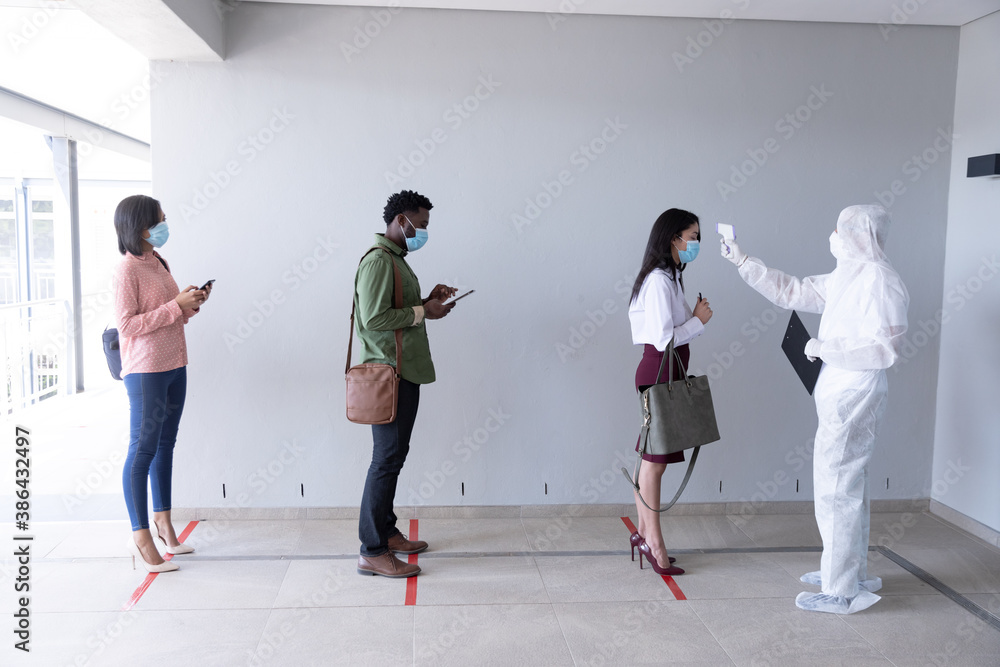 Fototapeta premium Health worker wearing protective clothes checking temperature of businesswoman